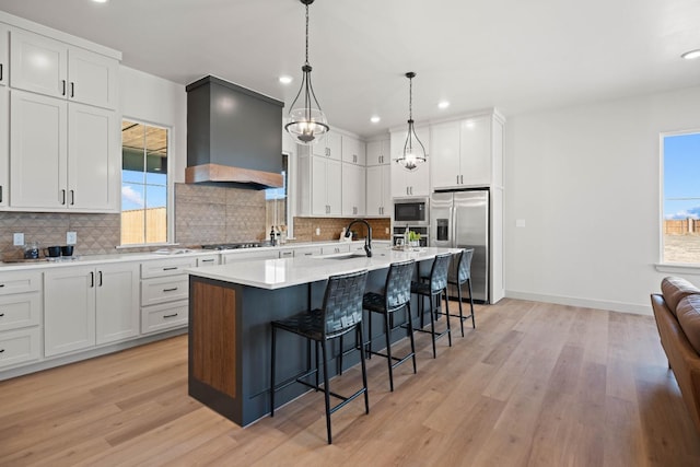 kitchen featuring a breakfast bar, stainless steel appliances, an island with sink, custom range hood, and white cabinets