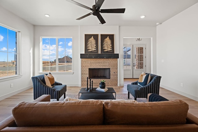 living room with a tiled fireplace, light hardwood / wood-style flooring, and ceiling fan