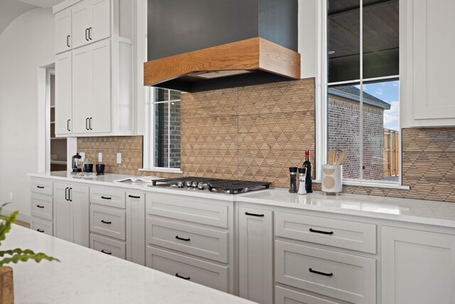 kitchen featuring custom exhaust hood, stainless steel gas cooktop, white cabinets, and decorative backsplash