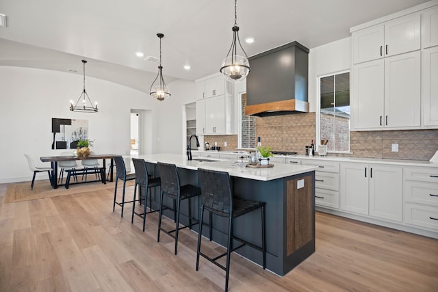 kitchen featuring custom exhaust hood, hanging light fixtures, a kitchen island with sink, and white cabinets