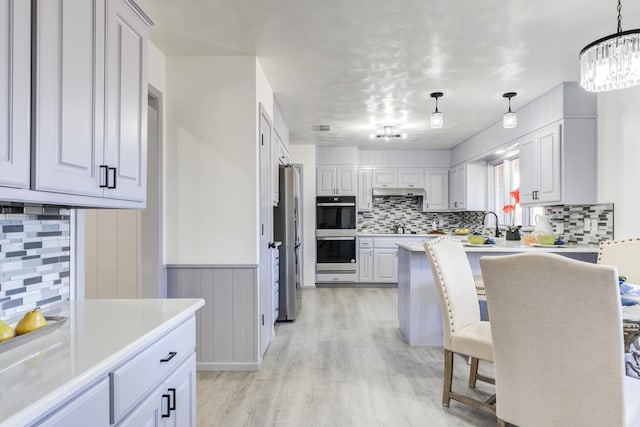kitchen featuring a breakfast bar, a chandelier, light wood-style flooring, decorative backsplash, and appliances with stainless steel finishes