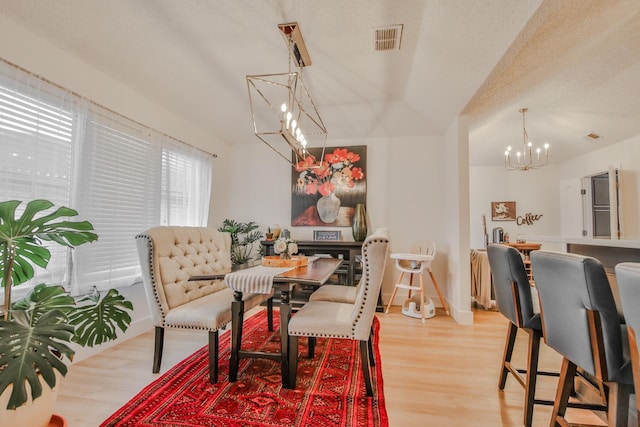 dining area with an inviting chandelier, light hardwood / wood-style floors, and a textured ceiling