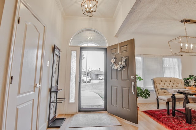 entrance foyer with an inviting chandelier, plenty of natural light, ornamental molding, and light wood-type flooring