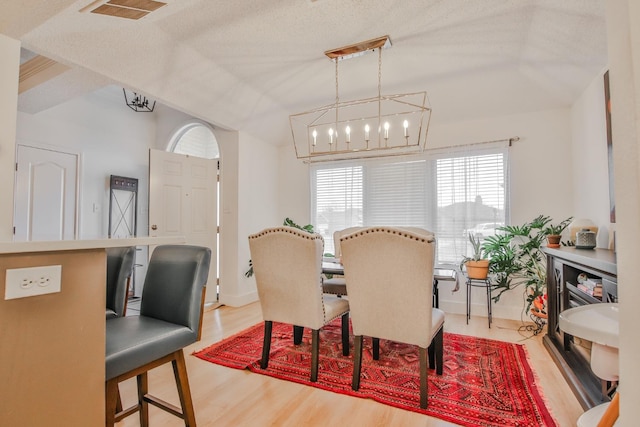 dining space featuring lofted ceiling, a healthy amount of sunlight, hardwood / wood-style floors, and a textured ceiling