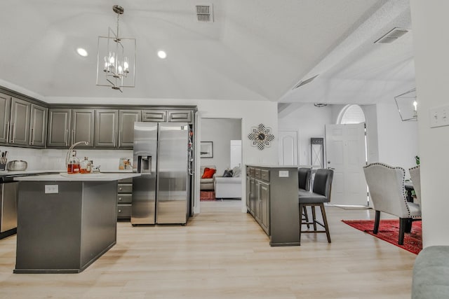 kitchen with a center island, vaulted ceiling, light wood-type flooring, a kitchen breakfast bar, and stainless steel fridge