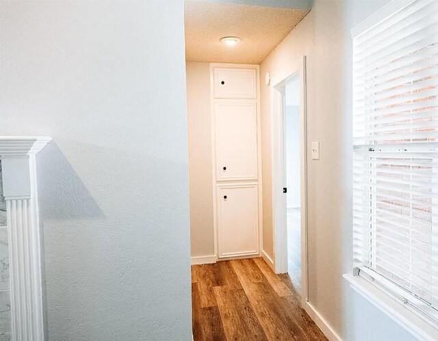 hall with a wealth of natural light, wood finished floors, baseboards, and a textured ceiling