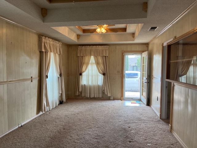 unfurnished room featuring wood walls, ornamental molding, light colored carpet, ceiling fan, and a tray ceiling