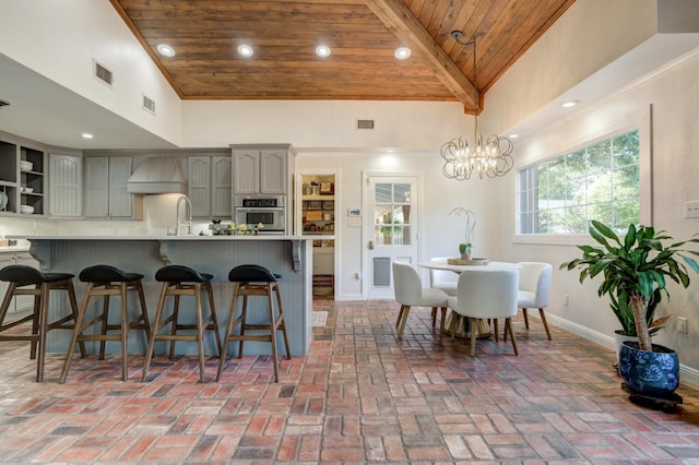 kitchen featuring gray cabinets, premium range hood, beamed ceiling, stainless steel oven, and wood ceiling