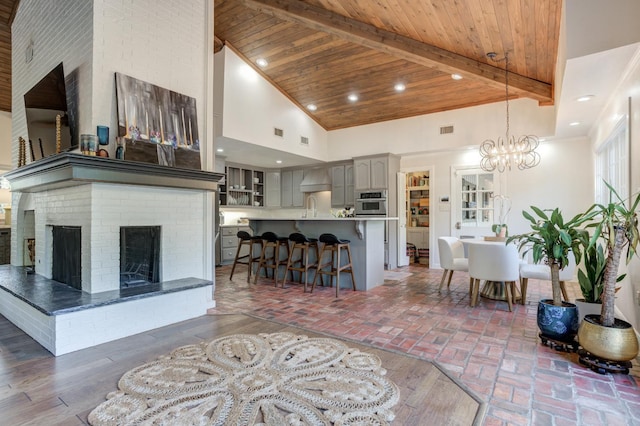 living room with beamed ceiling, a high ceiling, wood ceiling, a brick fireplace, and an inviting chandelier