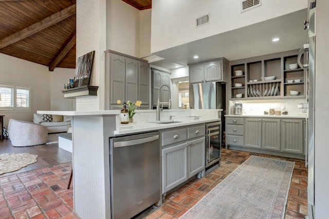 kitchen featuring stainless steel dishwasher, a kitchen breakfast bar, gray cabinets, beamed ceiling, and beverage cooler