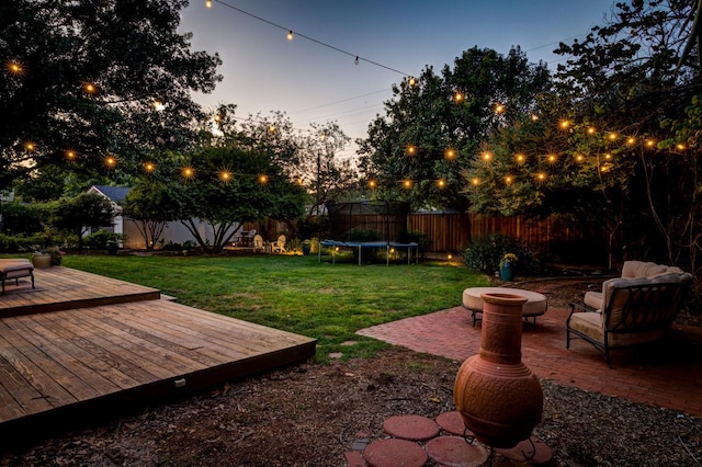 yard at dusk with a trampoline, a patio area, an outdoor fire pit, and a deck