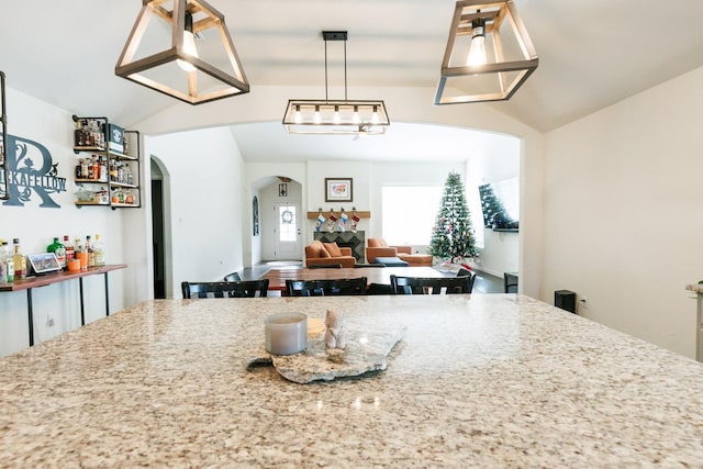 kitchen with light stone counters, vaulted ceiling, and hanging light fixtures