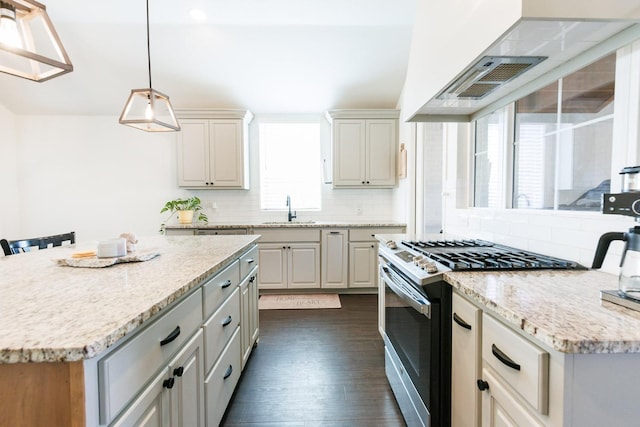 kitchen featuring sink, a breakfast bar area, stainless steel gas range oven, decorative light fixtures, and a kitchen island