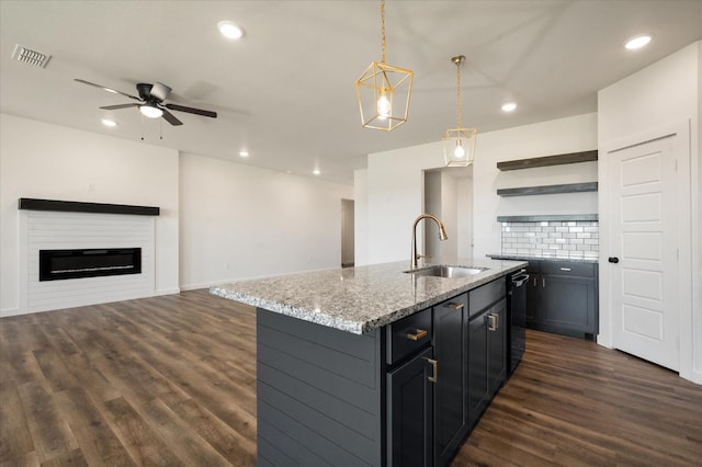 kitchen with sink, decorative backsplash, hanging light fixtures, a kitchen island with sink, and dark wood-type flooring