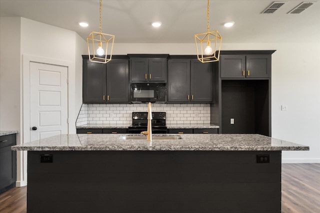 kitchen featuring light stone countertops, decorative light fixtures, black appliances, and a center island with sink