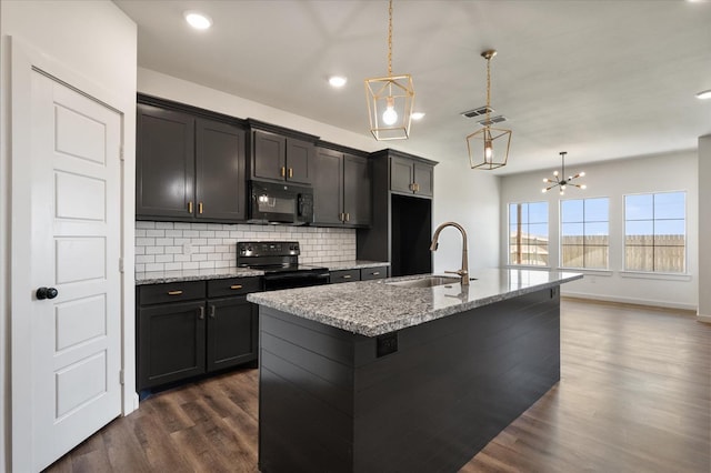 kitchen featuring decorative light fixtures, sink, a kitchen island with sink, light stone counters, and black appliances