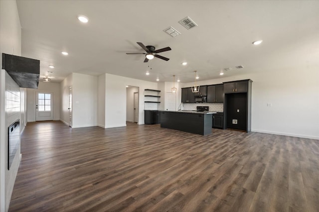 kitchen with a breakfast bar area, ceiling fan, a kitchen island with sink, dark hardwood / wood-style floors, and decorative backsplash