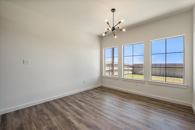 empty room with a healthy amount of sunlight, dark hardwood / wood-style flooring, and a chandelier