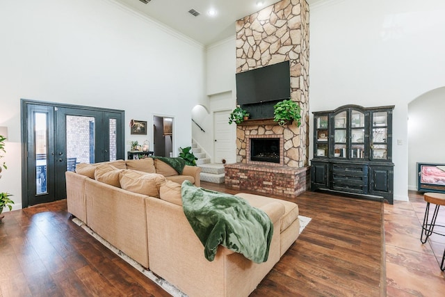 living room featuring crown molding, a towering ceiling, a stone fireplace, and dark hardwood / wood-style floors