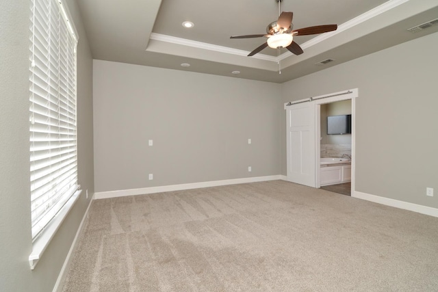 unfurnished room featuring ceiling fan, a tray ceiling, ornamental molding, light colored carpet, and a barn door