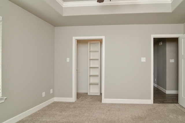 unfurnished bedroom with ornamental molding, a walk in closet, a tray ceiling, light carpet, and a closet