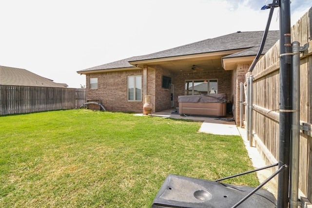 back of house with ceiling fan, a hot tub, and a lawn