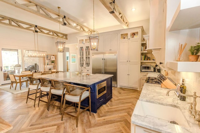 kitchen with white cabinetry, light parquet flooring, light stone countertops, and a center island with sink