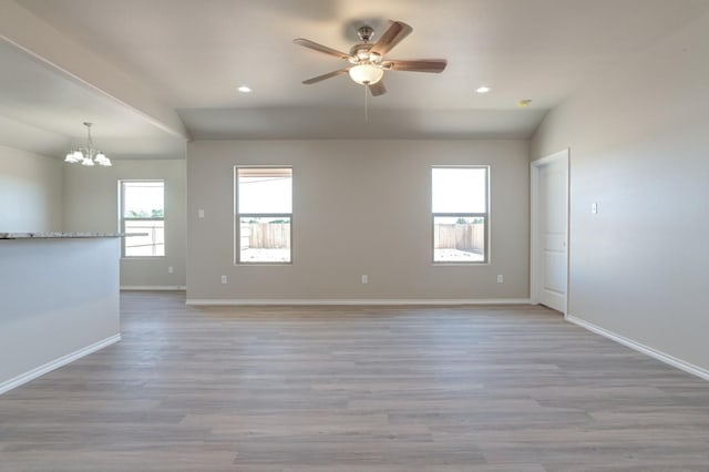 empty room with lofted ceiling, ceiling fan with notable chandelier, and light wood-type flooring