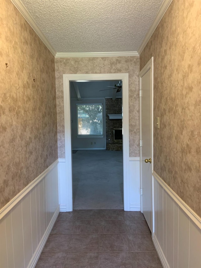 hall with dark tile patterned floors, ornamental molding, and a textured ceiling