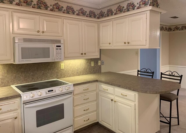 kitchen featuring white appliances, a breakfast bar, backsplash, ornamental molding, and kitchen peninsula