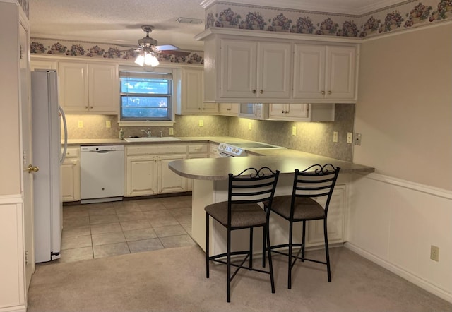 kitchen featuring sink, a breakfast bar area, white cabinetry, kitchen peninsula, and white appliances