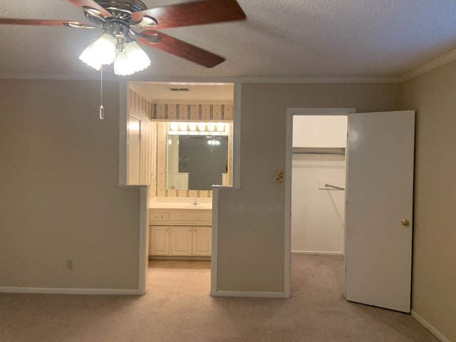 unfurnished bedroom with ensuite bathroom, sink, crown molding, a walk in closet, and light colored carpet