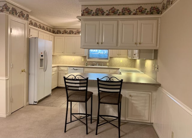 kitchen with white cabinetry, sink, a kitchen breakfast bar, white appliances, and a textured ceiling