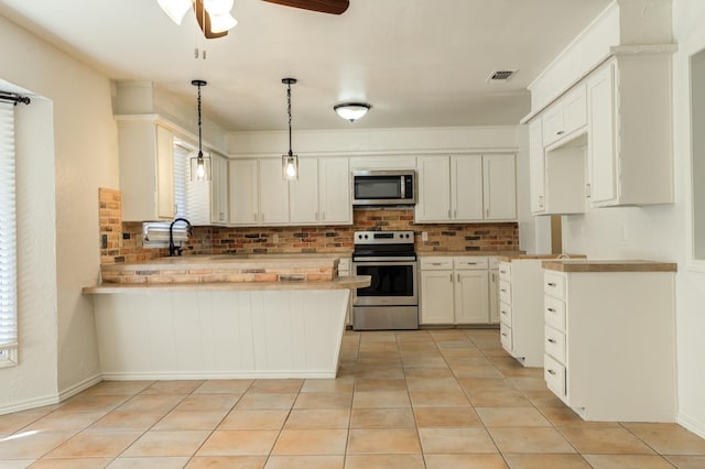 kitchen with light tile patterned floors, appliances with stainless steel finishes, backsplash, white cabinets, and decorative light fixtures