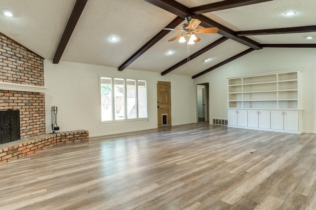 unfurnished living room featuring a fireplace, light hardwood / wood-style floors, a textured ceiling, and vaulted ceiling with beams