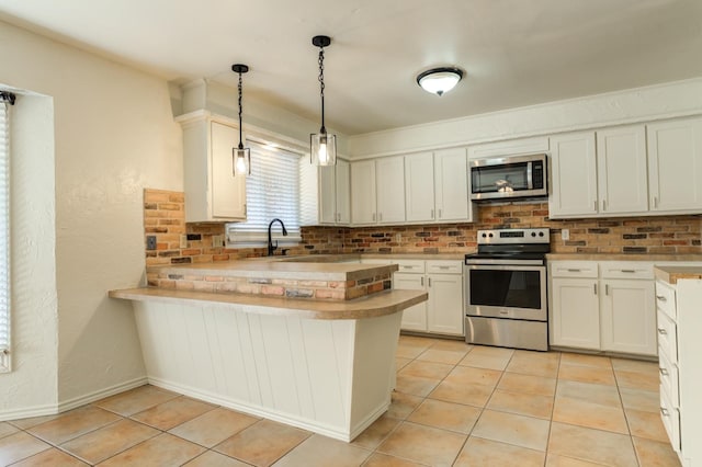 kitchen with light tile patterned flooring, appliances with stainless steel finishes, kitchen peninsula, and pendant lighting