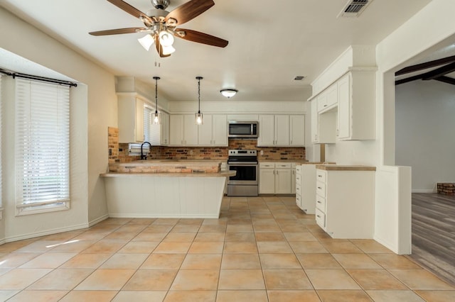 kitchen with pendant lighting, light tile patterned floors, stainless steel appliances, white cabinets, and kitchen peninsula