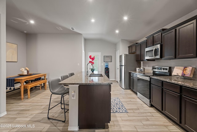 6827 38th St, Lubbock, TX 79407 - kitchen with appliances with stainless steel finishes, a center island with sink, a kitchen bar, light stone counters, and light wood-type flooring
