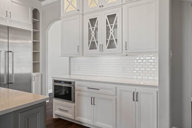 kitchen with appliances with stainless steel finishes, white cabinetry, backsplash, dark hardwood / wood-style flooring, and light stone countertops