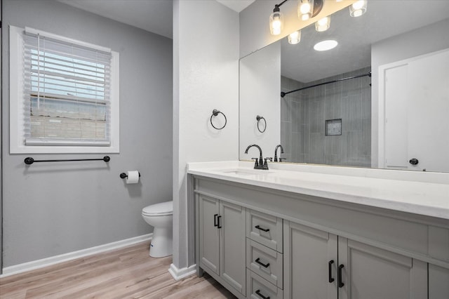 bathroom with vanity, toilet, hardwood / wood-style floors, and a tile shower