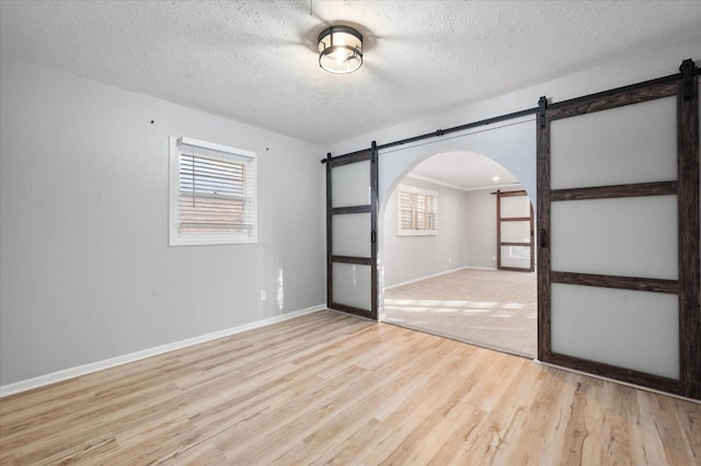 spare room featuring a barn door, a textured ceiling, and light wood-type flooring