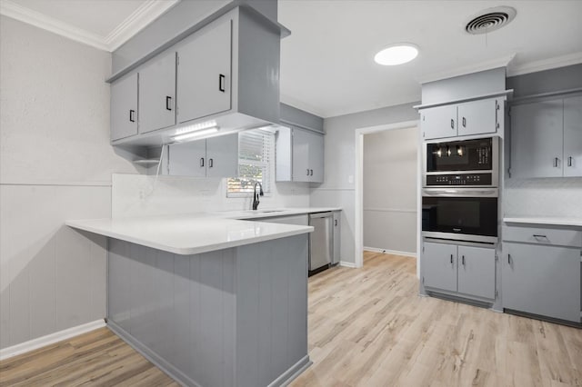 kitchen with gray cabinets, stainless steel appliances, kitchen peninsula, and light wood-type flooring