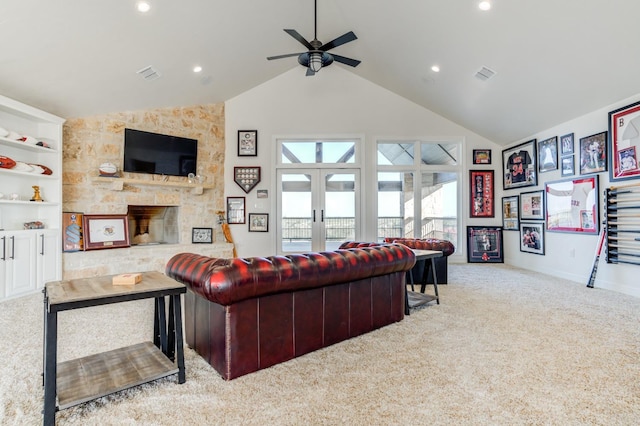 living room featuring ceiling fan, high vaulted ceiling, a stone fireplace, light colored carpet, and french doors