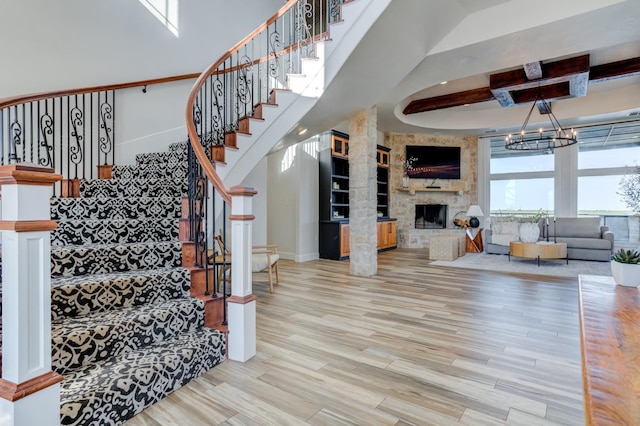 stairs with hardwood / wood-style flooring, a towering ceiling, a fireplace, and a notable chandelier