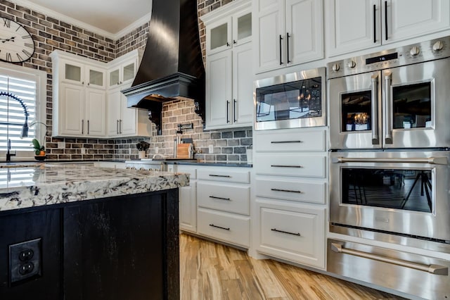 kitchen with built in microwave, double oven, custom exhaust hood, and white cabinets