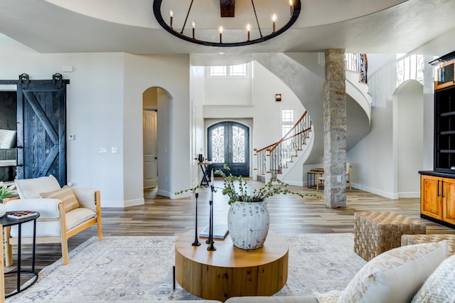 living room with a towering ceiling, a barn door, french doors, a chandelier, and light wood-type flooring