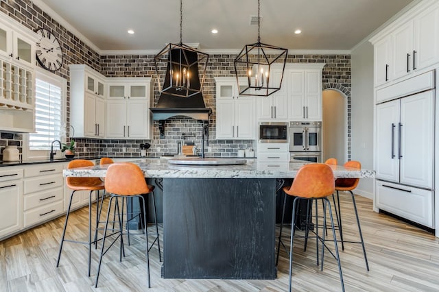 kitchen featuring premium range hood, a kitchen island, a kitchen breakfast bar, hanging light fixtures, and light stone counters