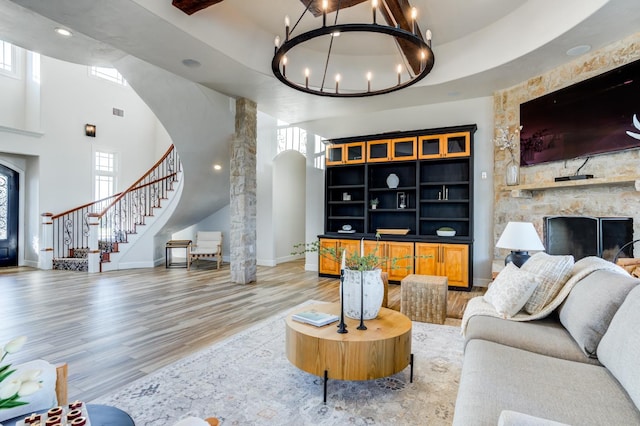 living room featuring ornate columns, a towering ceiling, hardwood / wood-style floors, a fireplace, and a chandelier