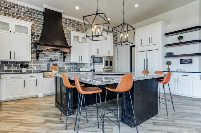 kitchen with white cabinetry, premium range hood, a kitchen island with sink, and dark stone countertops