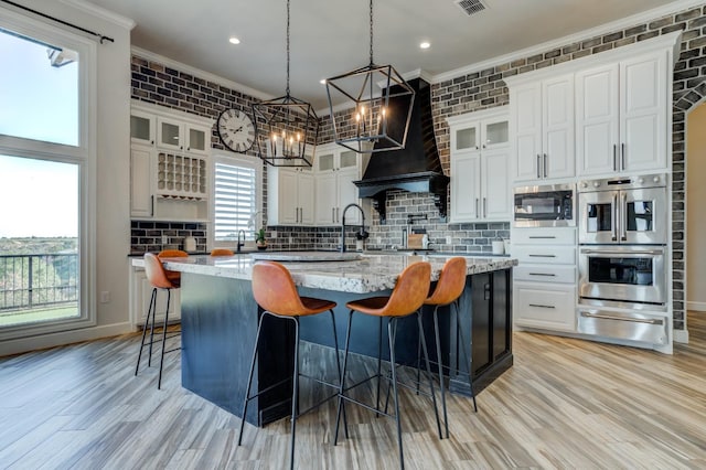 kitchen featuring built in microwave, light stone countertops, an island with sink, and white cabinets